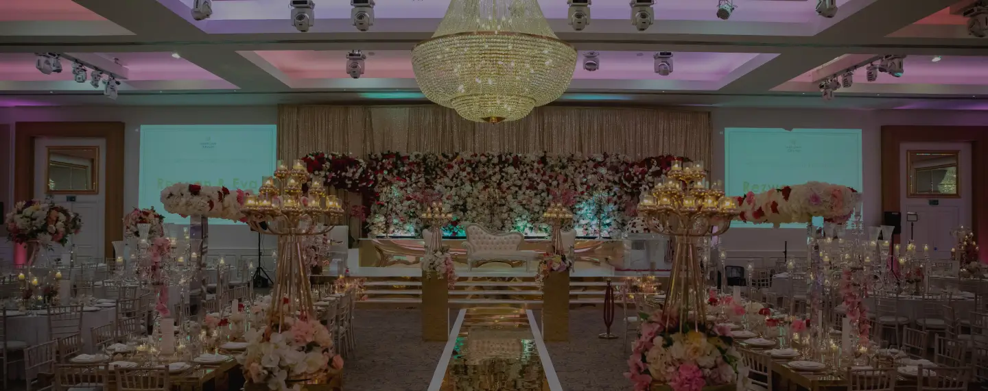 Ballroom with chandelier, gold florals and a white aisle at Meridian Grand — luxury wedding venue London.