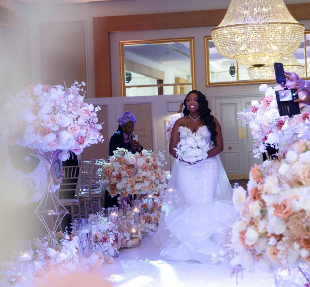 Bride walking down a flower-lined aisle beneath a crystal chandelier at Meridian Grand, North London