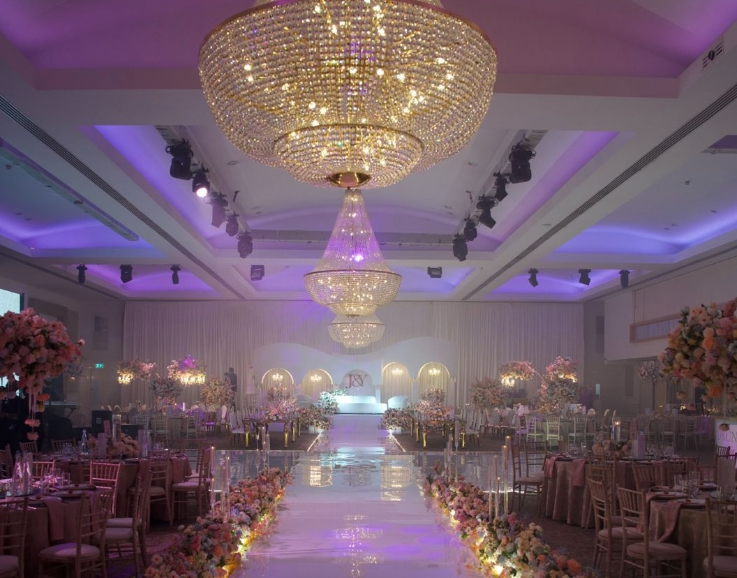 Ballroom at Meridian Grand set for a wedding reception, with crystal chandeliers, a lit aisle and floral table styling